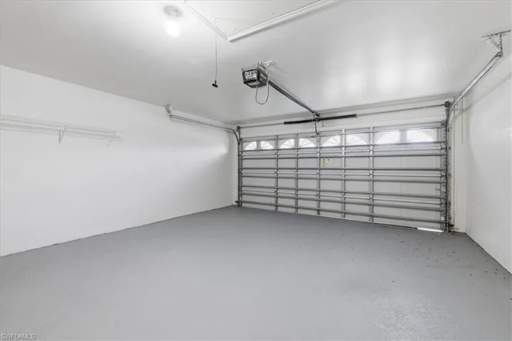 Attached garage featuring an automatic opener, overhead lighting, wire shelving, and a painted concrete floor