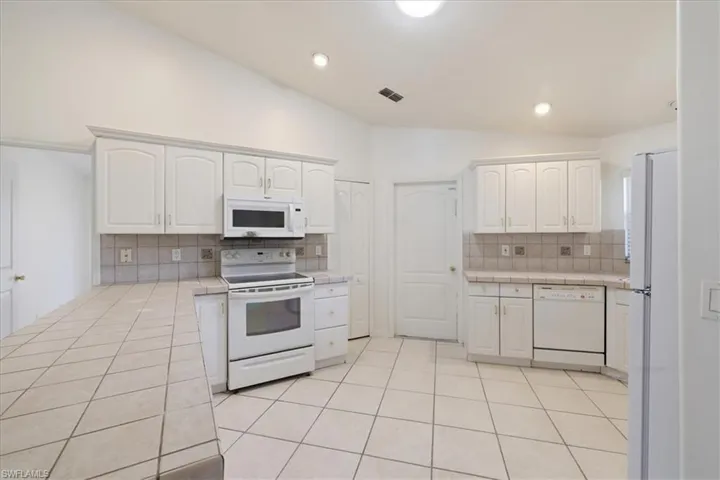 Kitchen featuring vaulted ceilings, white cabinetry, tile countertops, integrated appliances, and a diagonal tile floor