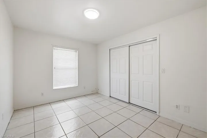 Room featuring white tile flooring, a window with horizontal blinds, and a built-in closet with white panel sliding doors