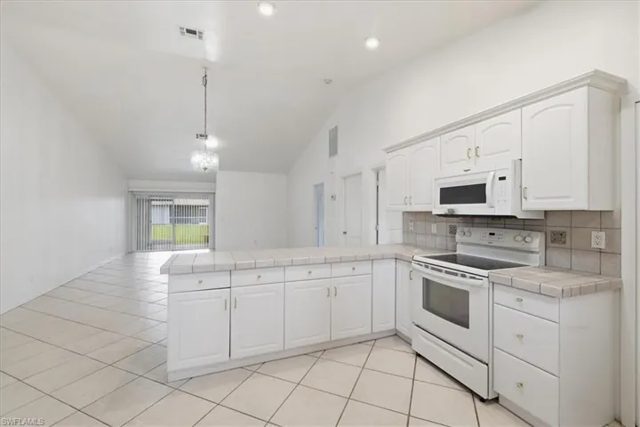 Kitchen featuring white cabinetry, tile countertops, and a white electric range with an overhead microwave