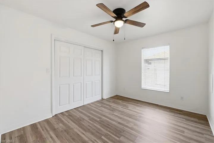 Interior space featuring wood-finish flooring, a ceiling fan with integrated lighting, and a window with horizontal blinds