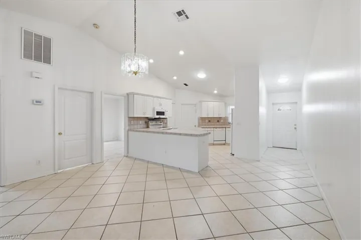Open-concept living space featuring vaulted ceilings, tile flooring throughout, and a kitchen with white cabinetry, a built-in microwave, and a tile backsplash