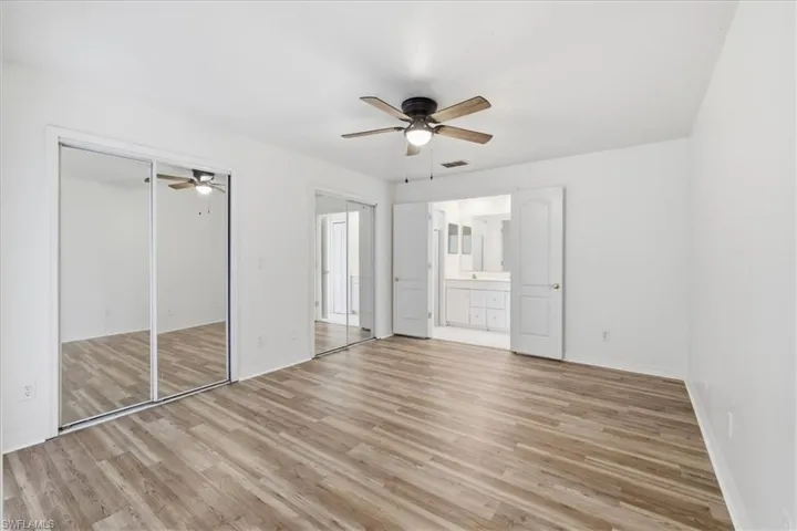 Spacious room featuring wood-finish flooring, a ceiling fan with integrated lighting, and mirrored sliding closet doors
