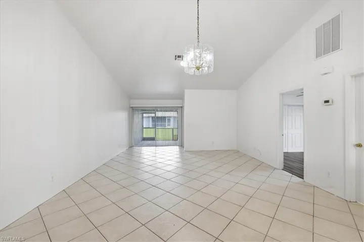Spacious interior with vaulted ceilings, featuring neutral-toned tile flooring, a decorative chandelier, and sliding glass doors leading to an outdoor area