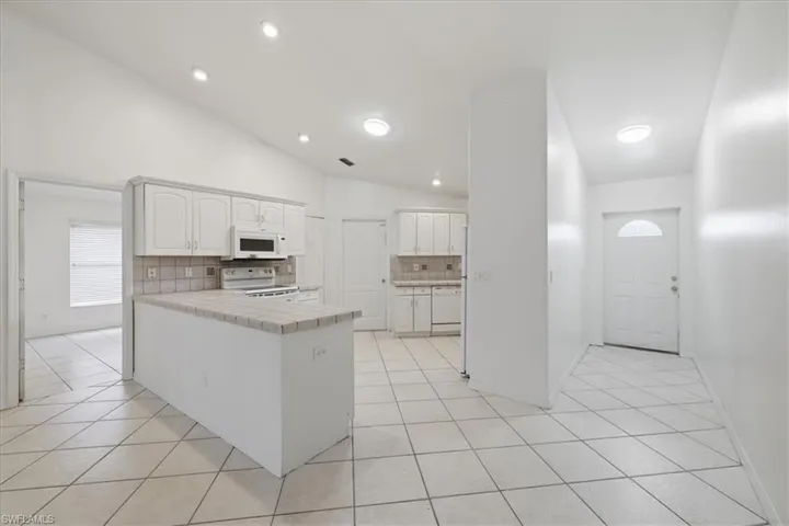 Bright kitchen featuring white cabinetry, tile countertops, recessed lighting, and a vaulted ceiling