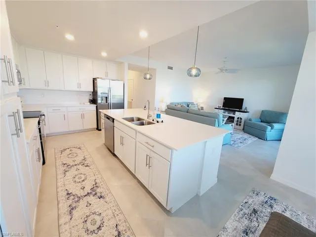 Kitchen with stainless steel appliances, ceiling fan, sink, a center island with sink, and white cabinets