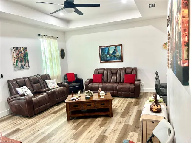 Living room featuring ceiling fan, light hardwood / wood-style flooring, and a tray ceiling