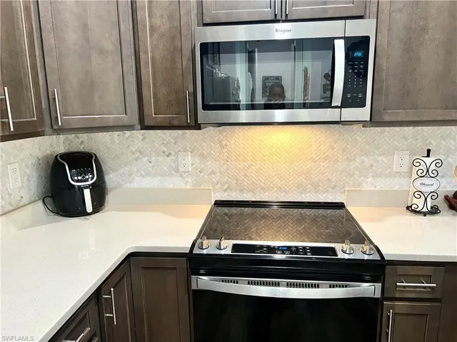 Kitchen with dark brown cabinets, electric range, and tasteful backsplash