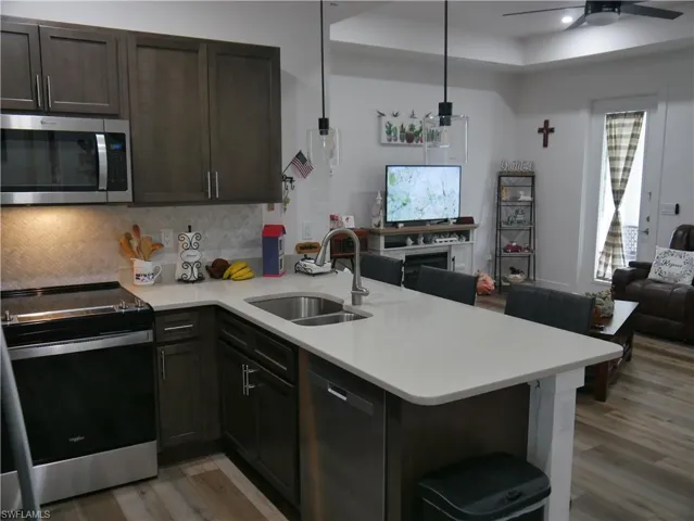 Kitchen with appliances with stainless steel finishes, hardwood / wood-style flooring, kitchen peninsula, sink, and ceiling fan