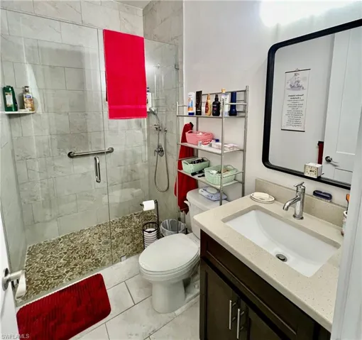 Bathroom featuring walk in shower, tile flooring, vanity, and toilet