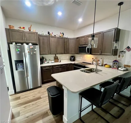 Kitchen with light hardwood / wood-style floors, a kitchen breakfast bar, stainless steel appliances, kitchen peninsula, and pendant lighting