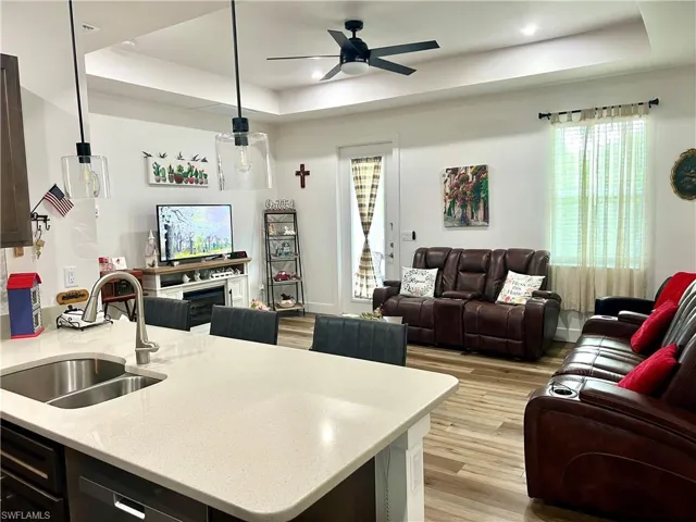 Kitchen featuring light hardwood / wood-style floors, pendant lighting, sink, ceiling fan, and a raised ceiling
