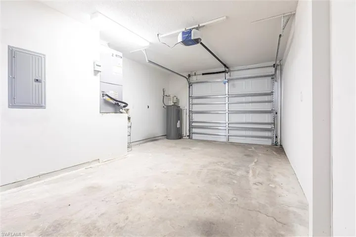 Garage featuring electric panel, water heater, a garage door opener, and heating unit