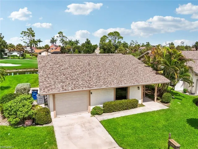 View of front facade featuring a shingled roof, a front lawn, stucco siding, and concrete driveway