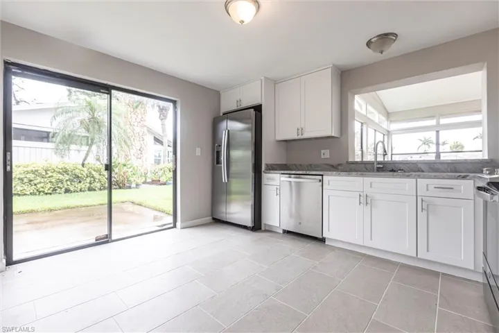 Kitchen featuring stainless steel appliances, white cabinetry, and light stone counters