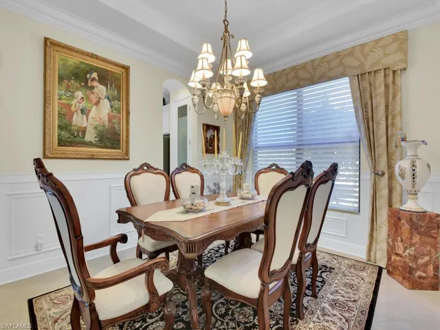Dining space featuring arched walkways, a chandelier, crown molding, a decorative wall, and wainscoting