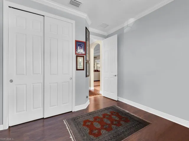 Unfurnished bedroom with arched walkways, wood finished floors, crown molding, and a closet
