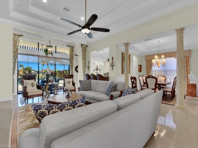 Living area featuring decorative columns, a tray ceiling, ornamental molding, a chandelier, and ceiling fan