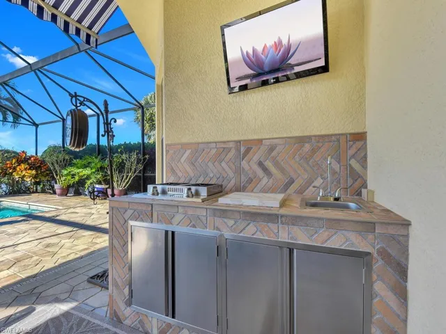 View of patio with an outdoor kitchen, glass enclosure, and an outdoor pool