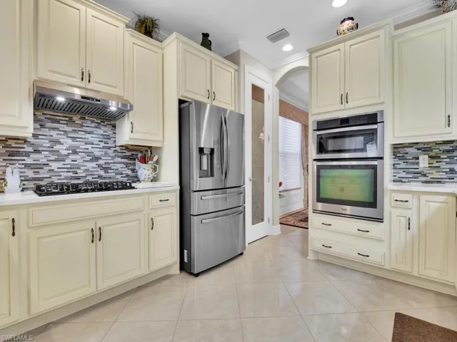 Kitchen with appliances with stainless steel finishes, cream cabinets, under cabinet range hood, crown molding, and decorative backsplash