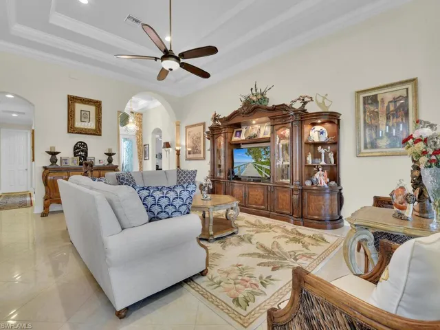 Living area with arched walkways, ceiling fan, crown molding, a tray ceiling, and recessed lighting