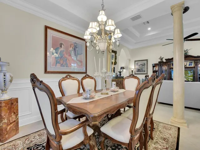 Dining area featuring ornate columns, crown molding, a chandelier, wainscoting, and light tile patterned floors