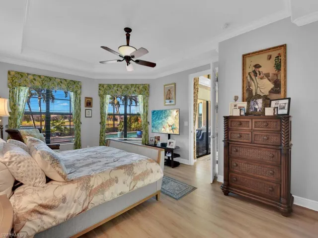 Bedroom featuring light wood-type flooring, ornamental molding, a raised ceiling, and a ceiling fan