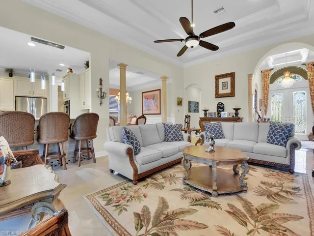 Living room featuring ceiling fan, arched walkways, french doors, ornamental molding, and ornate columns