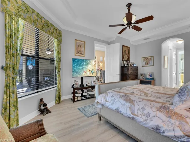 Bedroom featuring arched walkways, wood finished floors, ornamental molding, a ceiling fan, and multiple windows