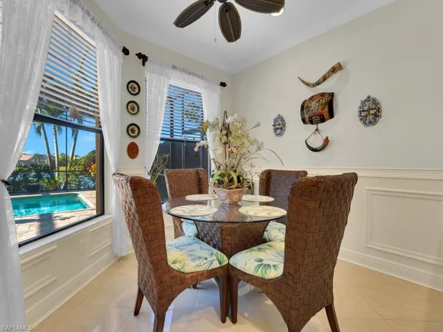 Dining area featuring a decorative wall, light tile patterned flooring, ceiling fan, wainscoting, and crown molding
