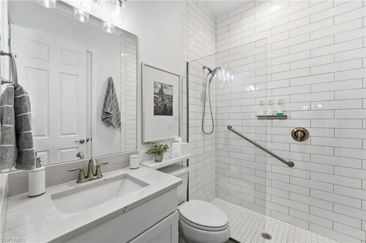 The second bathroom serves as the ensuite for the second bedroom and features a walk-in shower with floor-to-ceiling subway tile and a seamless glass enclosure, complemented by a white quartz countertop and stunning lighting.