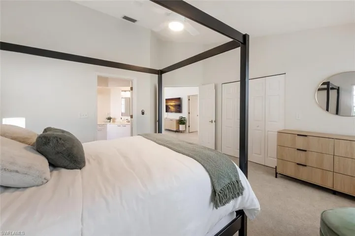 Bedroom with light colored carpet, ceiling fan, connected bathroom, high vaulted ceiling, and two closets