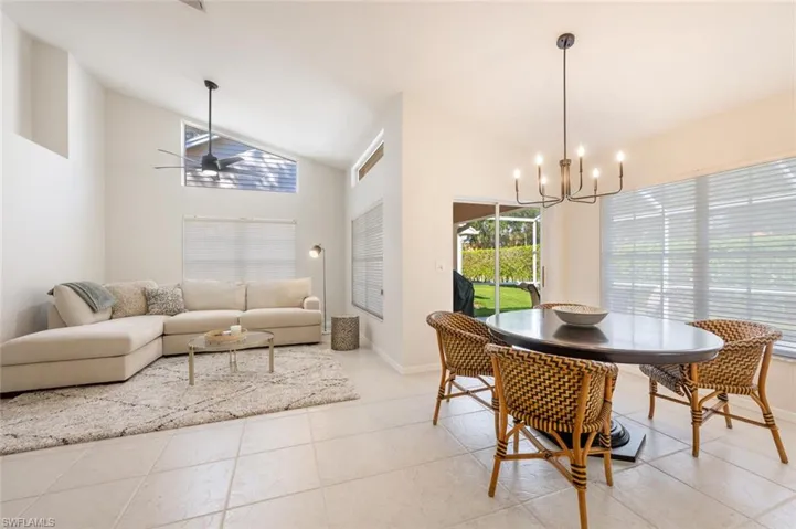 Dining space featuring light tile patterned flooring, high vaulted ceiling, and ceiling fan with notable chandelier
