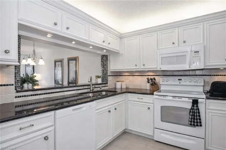 Kitchen with white appliances, dark stone countertops, and white cabinetry