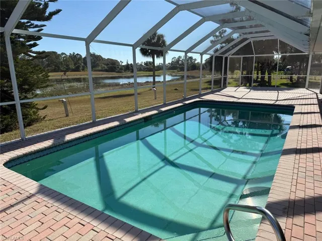 Swimming pool with a sunroom, glass enclosure, a water view, and a yard