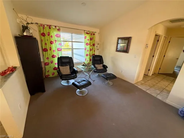 Sitting room featuring vaulted ceiling, light colored carpet, and arched walkways