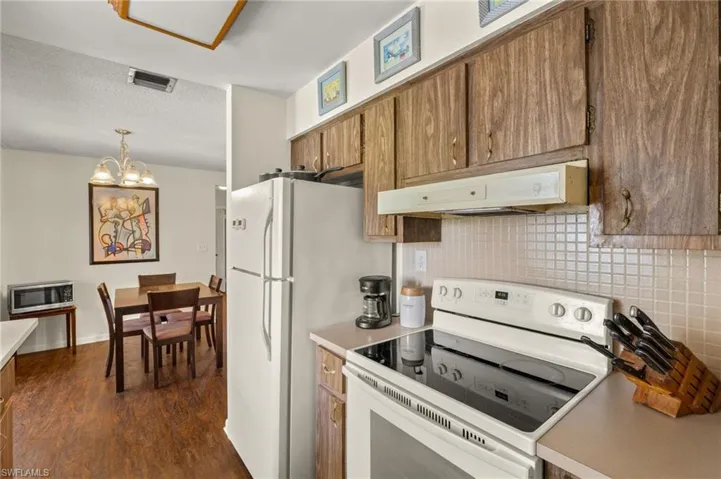 Kitchen featuring white appliances, under cabinet range hood, brown cabinetry, backsplash, and dark wood-style flooring