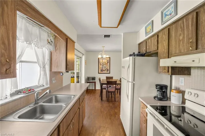 Kitchen with white electric range oven, brown cabinetry, a chandelier, and dark wood-type flooring