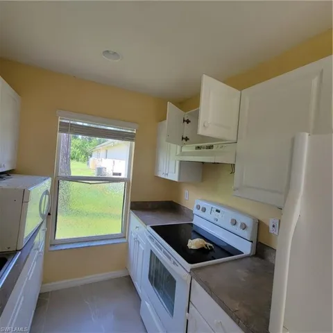 Kitchen with white appliances, white cabinetry, dark countertops, light tile patterned flooring, and exhaust hood