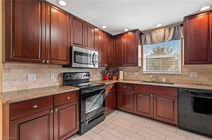 Kitchen with tasteful backsplash, light stone countertops, sink, and black appliances