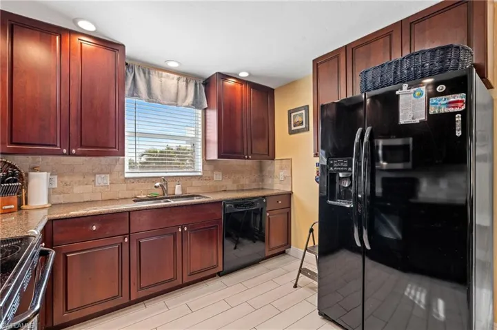Kitchen with light stone countertops, sink, backsplash, and black appliances