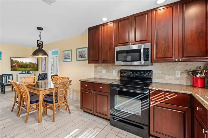 Kitchen featuring pendant lighting, black electric range oven, backsplash, light stone countertops, and light hardwood / wood-style floors