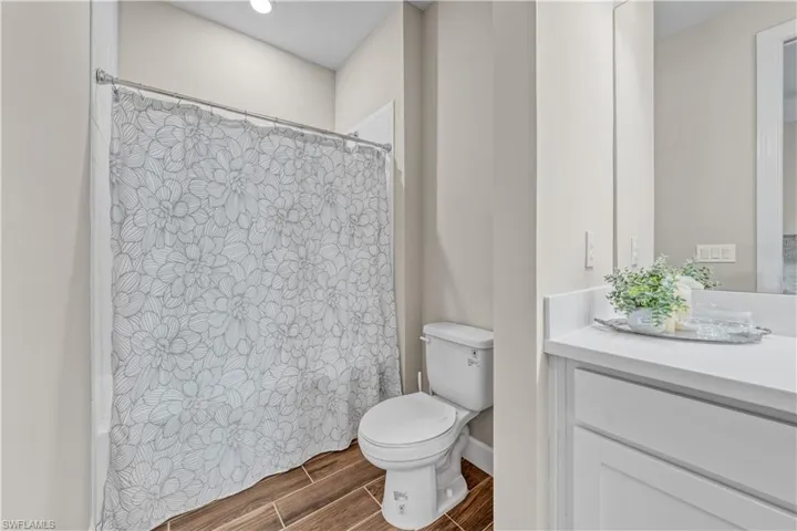 Bathroom featuring a white vanity with a light-colored countertop, wood-finish tile flooring, and a shower with a patterned curtain