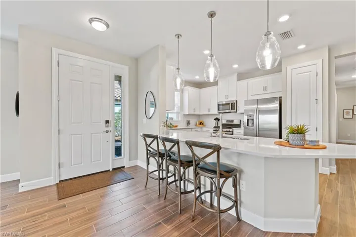 Open-concept kitchen featuring white cabinetry, stainless steel appliances, a large center island with a quartz-finish countertop, and wood-finish flooring throughout