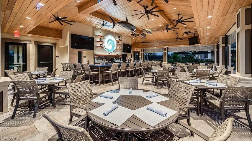 Expansive covered patio featuring a vaulted wood-finish ceiling, multiple ceiling fans, an integrated bar area with bar seating, and ample dining space
