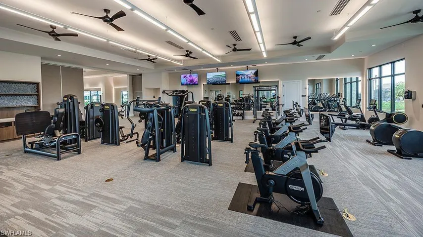 Spacious fitness center featuring modern exercise equipment, large windows, recessed lighting, ceiling fans, and patterned carpet flooring