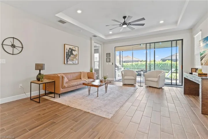 Spacious living area featuring wood-finish tile flooring, a tray ceiling with recessed lighting and a ceiling fan, and expansive sliding glass doors leading to a screened lanai