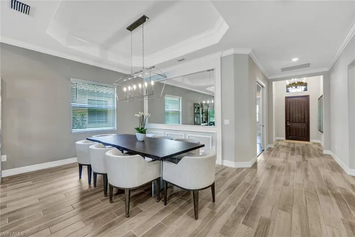 Dining space with a tray ceiling, ornamental molding, a chandelier, and light hardwood / wood-style flooring