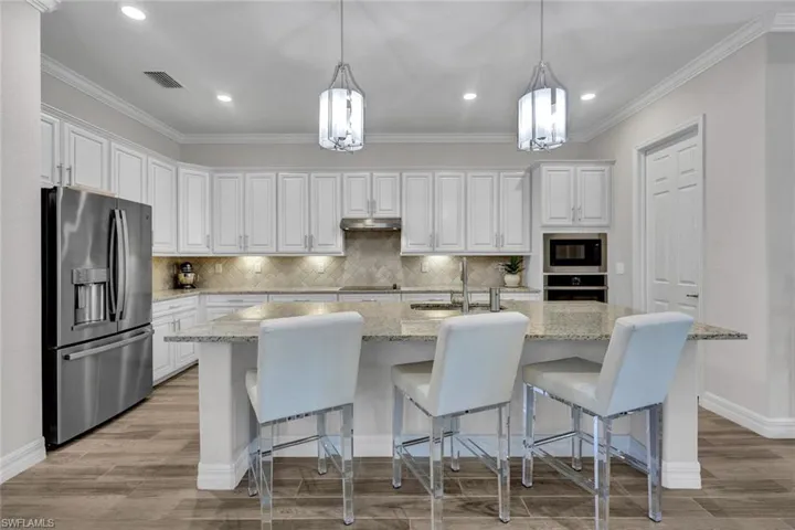 Kitchen featuring hanging light fixtures, stainless steel fridge, a center island with sink, light hardwood / wood-style flooring, and backsplash