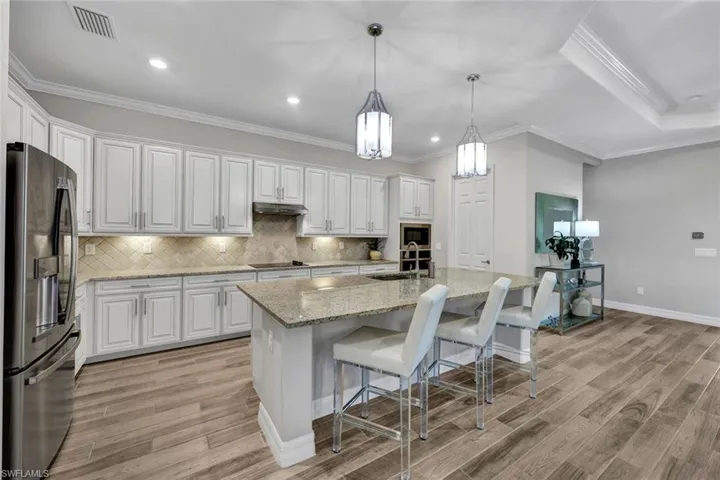 Kitchen with ornamental molding, white cabinets, light wood-type flooring, and stainless steel fridge with ice dispenser